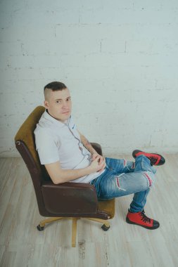Duygusal ofis çalışanı dövmeli, beyaz duvara karşı bir sandalye üzerinde oturan adam. Bir kravat adam kot pantolon ve beyaz gömlek giymiş.
