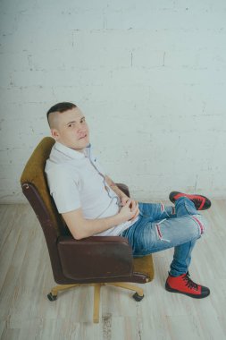 Duygusal ofis çalışanı dövmeli, beyaz duvara karşı bir sandalye üzerinde oturan adam. Bir kravat adam kot pantolon ve beyaz gömlek giymiş.