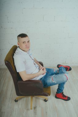 Duygusal ofis çalışanı dövmeli, beyaz duvara karşı bir sandalye üzerinde oturan adam. Bir kravat adam kot pantolon ve beyaz gömlek giymiş.