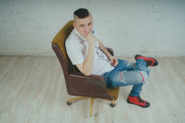 Duygusal ofis çalışanı dövmeli, beyaz duvara karşı bir sandalye üzerinde oturan adam. Bir kravat adam kot pantolon ve beyaz gömlek giymiş.