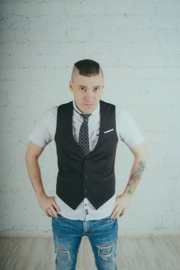 Beyaz duvara karşı poz duygusal ofis çalışanı ile bir dövme. Bir kravat adam kot pantolon ve beyaz gömlek giymiş.