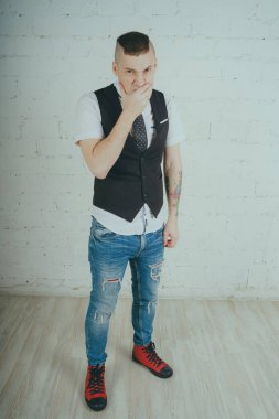 Beyaz duvara karşı poz duygusal ofis çalışanı ile bir dövme. Bir kravat adam kot pantolon ve beyaz gömlek giymiş.