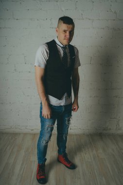 Beyaz duvara karşı poz duygusal ofis çalışanı ile bir dövme. Bir kravat adam kot pantolon ve beyaz gömlek giymiş.