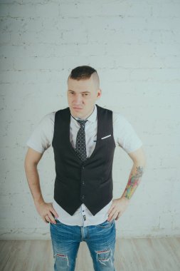 Beyaz duvara karşı poz duygusal ofis çalışanı ile bir dövme. Bir kravat adam kot pantolon ve beyaz gömlek giymiş.