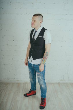 Beyaz duvara karşı poz duygusal ofis çalışanı ile bir dövme. Bir kravat adam kot pantolon ve beyaz gömlek giymiş.