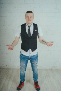 Beyaz duvara karşı poz duygusal ofis çalışanı ile bir dövme. Bir kravat adam kot pantolon ve beyaz gömlek giymiş.