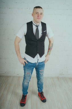 Beyaz duvara karşı poz duygusal ofis çalışanı ile bir dövme. Bir kravat adam kot pantolon ve beyaz gömlek giymiş.