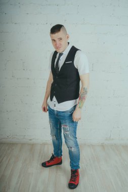 Beyaz duvara karşı poz duygusal ofis çalışanı ile bir dövme. Bir kravat adam kot pantolon ve beyaz gömlek giymiş.