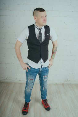 Beyaz duvara karşı poz duygusal ofis çalışanı ile bir dövme. Bir kravat adam kot pantolon ve beyaz gömlek giymiş.