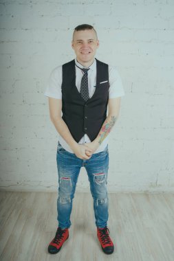 Beyaz duvara karşı poz duygusal ofis çalışanı ile bir dövme. Bir kravat adam kot pantolon ve beyaz gömlek giymiş.