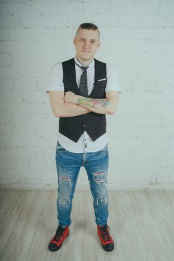 Beyaz duvara karşı poz duygusal ofis çalışanı ile bir dövme. Bir kravat adam kot pantolon ve beyaz gömlek giymiş.