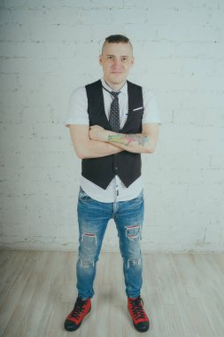 Beyaz duvara karşı poz duygusal ofis çalışanı ile bir dövme. Bir kravat adam kot pantolon ve beyaz gömlek giymiş.