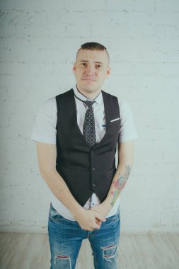 Beyaz duvara karşı poz duygusal ofis çalışanı ile bir dövme. Bir kravat adam kot pantolon ve beyaz gömlek giymiş.