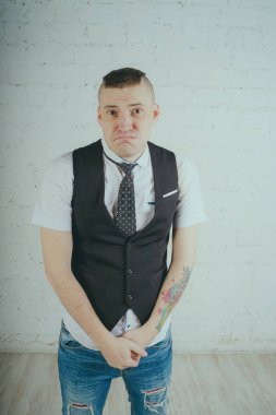 Beyaz duvara karşı poz duygusal ofis çalışanı ile bir dövme. Bir kravat adam kot pantolon ve beyaz gömlek giymiş.