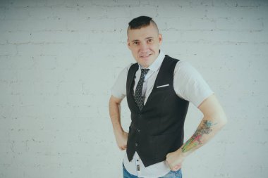 Beyaz duvara karşı poz duygusal ofis çalışanı ile bir dövme. Bir kravat adam kot pantolon ve beyaz gömlek giymiş.