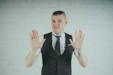 Beyaz duvara karşı poz duygusal ofis çalışanı ile bir dövme. Bir kravat adam kot pantolon ve beyaz gömlek giymiş.