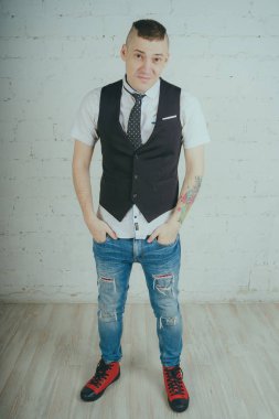 Beyaz duvara karşı poz duygusal ofis çalışanı ile bir dövme. Bir kravat adam kot pantolon ve beyaz gömlek giymiş.