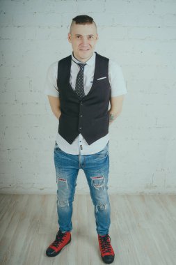 Beyaz duvara karşı poz duygusal ofis çalışanı ile bir dövme. Bir kravat adam kot pantolon ve beyaz gömlek giymiş.