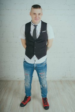 Beyaz duvara karşı poz duygusal ofis çalışanı ile bir dövme. Bir kravat adam kot pantolon ve beyaz gömlek giymiş.