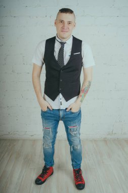 Beyaz duvara karşı poz duygusal ofis çalışanı ile bir dövme. Bir kravat adam kot pantolon ve beyaz gömlek giymiş.