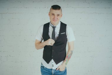 Beyaz duvara karşı poz duygusal ofis çalışanı ile bir dövme. Bir kravat adam kot pantolon ve beyaz gömlek giymiş.