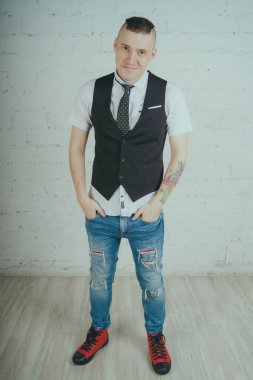 Beyaz duvara karşı poz duygusal ofis çalışanı ile bir dövme. Bir kravat adam kot pantolon ve beyaz gömlek giymiş.