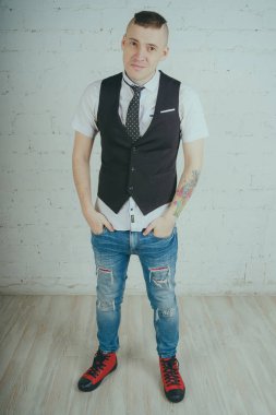 Beyaz duvara karşı poz duygusal ofis çalışanı ile bir dövme. Bir kravat adam kot pantolon ve beyaz gömlek giymiş.