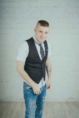 Beyaz duvara karşı poz duygusal ofis çalışanı ile bir dövme. Bir kravat adam kot pantolon ve beyaz gömlek giymiş.