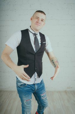 Beyaz duvara karşı poz duygusal ofis çalışanı ile bir dövme. Bir kravat adam kot pantolon ve beyaz gömlek giymiş.