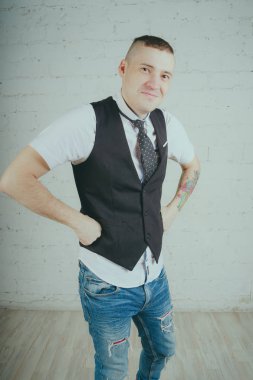 Beyaz duvara karşı poz duygusal ofis çalışanı ile bir dövme. Bir kravat adam kot pantolon ve beyaz gömlek giymiş.