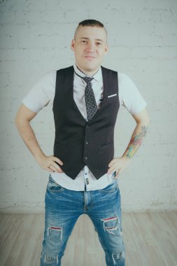 Beyaz duvara karşı poz duygusal ofis çalışanı ile bir dövme. Bir kravat adam kot pantolon ve beyaz gömlek giymiş.