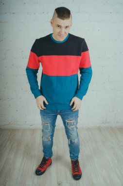 Yakışıklı olan bir tuğla duvara poz. Çizgili kazağı deli adam