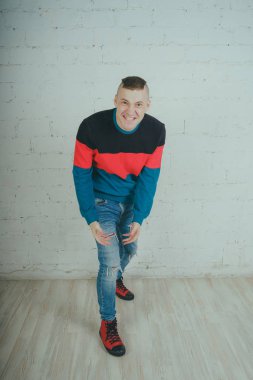 Yakışıklı olan bir tuğla duvara poz. Çizgili kazağı deli adam