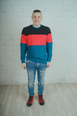 Yakışıklı olan bir tuğla duvara poz. Çizgili kazağı deli adam