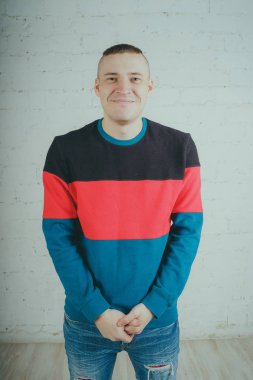 Yakışıklı olan bir tuğla duvara poz. Çizgili kazağı deli adam