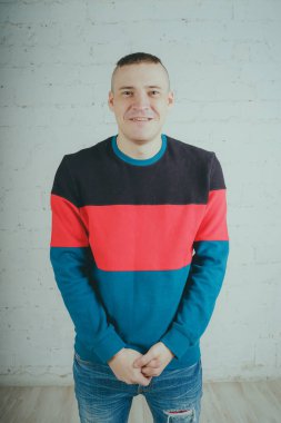 Yakışıklı olan bir tuğla duvara poz. Çizgili kazağı deli adam