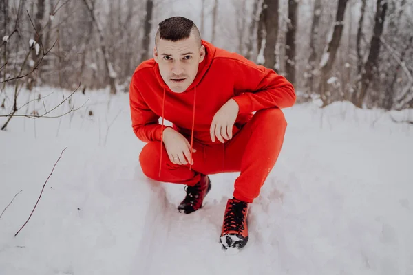 Crazy guy posing in the forest in the winter, on the background of snow and trees. A man in a red tracksuit walking in the fresh air. Concept: walking and training outdoors in the cold