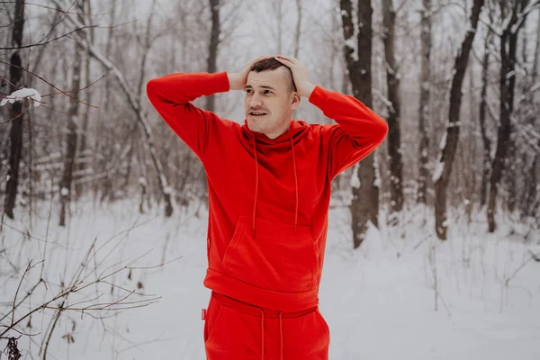 Crazy guy posing in the forest in the winter, on the background of snow and trees. A man in a red tracksuit walking in the fresh air. Concept: walking and training outdoors in the cold
