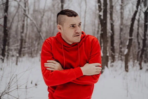 Crazy guy posing in the forest in the winter, on the background of snow and trees. A man in a red tracksuit walking in the fresh air. Concept: walking and training outdoors in the cold