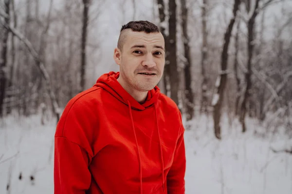 Crazy guy posing in the forest in the winter, on the background of snow and trees. A man in a red tracksuit walking in the fresh air. Concept: walking and training outdoors in the cold