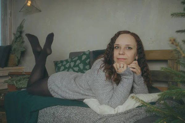 Kış konsepti. Bir gri örgü kazak sevimli genç kız. Güzel bir kadın beyaz bir yatak odasında rahatlatıcı bir şey. Elbise güzel kadınların sabah uyanıyor. Bir kazak giyen kadın