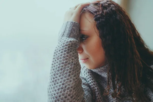 Genç bir kız bir kazaklı pencerenin önünde poz. Sıcak kazak giymiş kadın sokak stil giyim. Temiz cilt, uzun saç