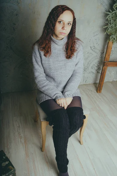 Gri bir duvara poz bir kazak bir genç kız. Sıcak kazak giymiş kadın sokak stil giyim. Temiz cilt, uzun saç