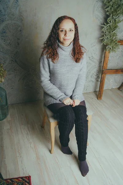 Gri bir duvara poz bir kazak bir genç kız. Sıcak kazak giymiş kadın sokak stil giyim. Temiz cilt, uzun saç