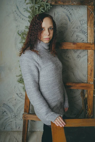 一个穿着毛衣的年轻女孩 靠在灰色的墙上 女人穿着暖和的毛衣 街头风格的衣服 干净的皮肤 — 图库照片