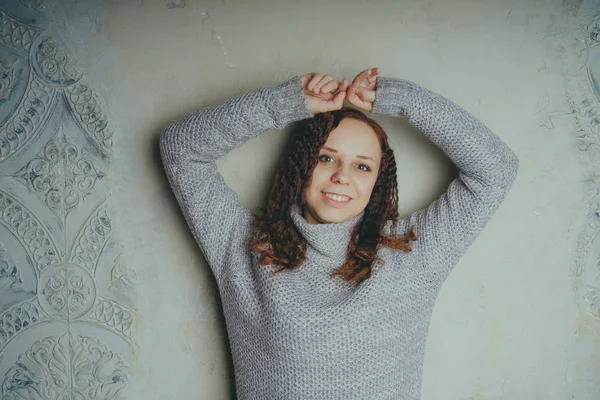 Gri bir duvara poz bir kazak bir genç kız. Sıcak kazak giymiş kadın sokak stil giyim. Temiz cilt, uzun saç