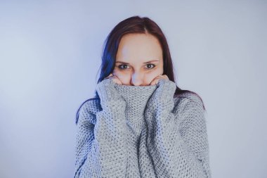 Gri bir duvara poz bir kazak bir genç kız. Sıcak kazak giymiş kadın sokak stil giyim. Temiz cilt, uzun saç