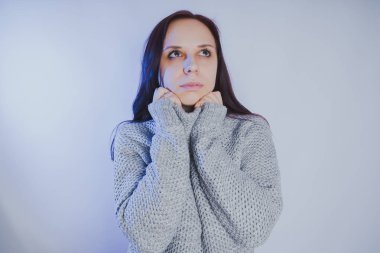 Gri bir duvara poz bir kazak bir genç kız. Sıcak kazak giymiş kadın sokak stil giyim. Temiz cilt, uzun saç