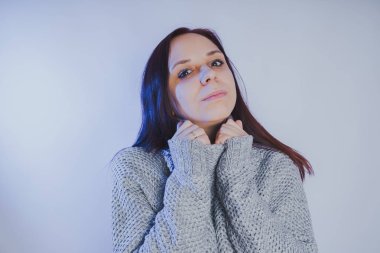 Gri bir duvara poz bir kazak bir genç kız. Sıcak kazak giymiş kadın sokak stil giyim. Temiz cilt, uzun saç