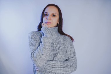 Gri bir duvara poz bir kazak bir genç kız. Sıcak kazak giymiş kadın sokak stil giyim. Temiz cilt, uzun saç